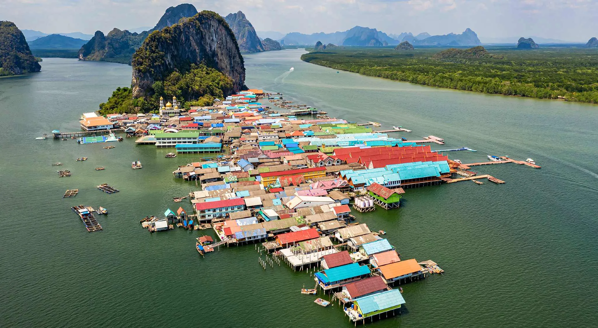 Floating wooden village on stilts in Phang Nga Bay with limestone cliff background